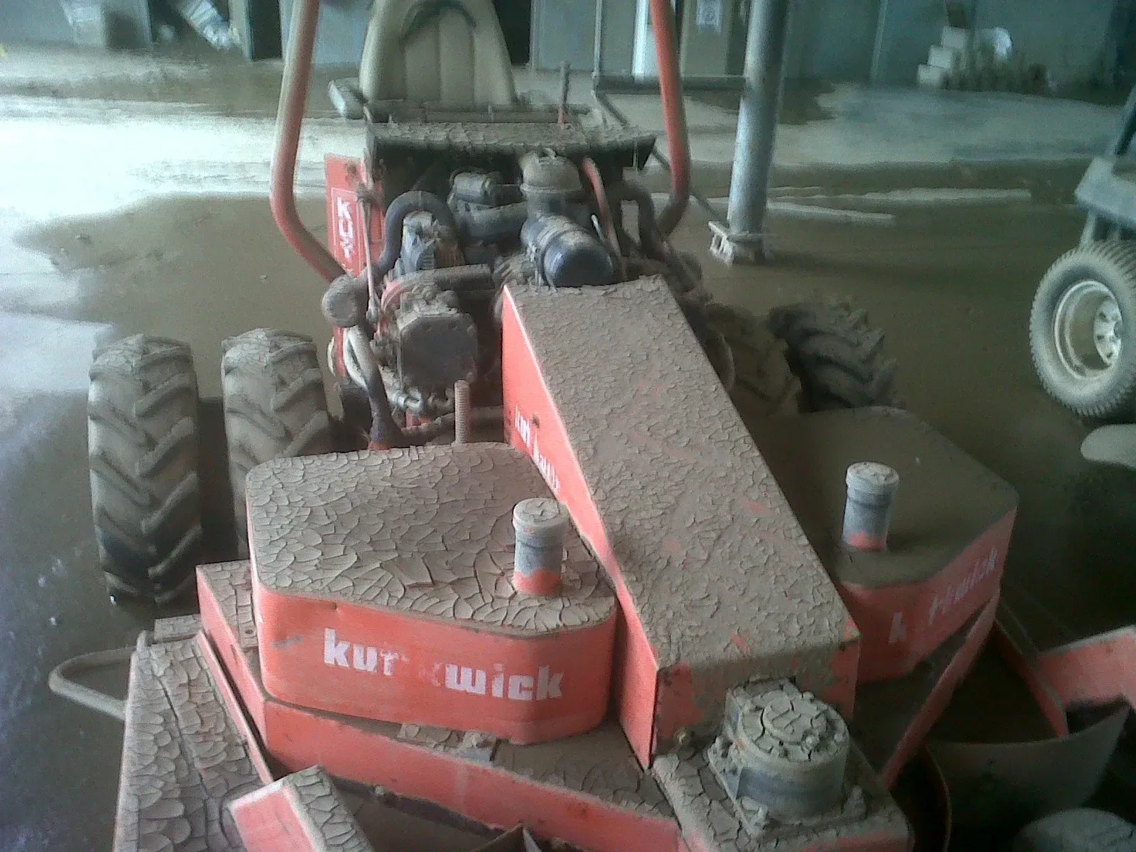 Red and dirty Kurwick lawn mower in a wet indoor setting.