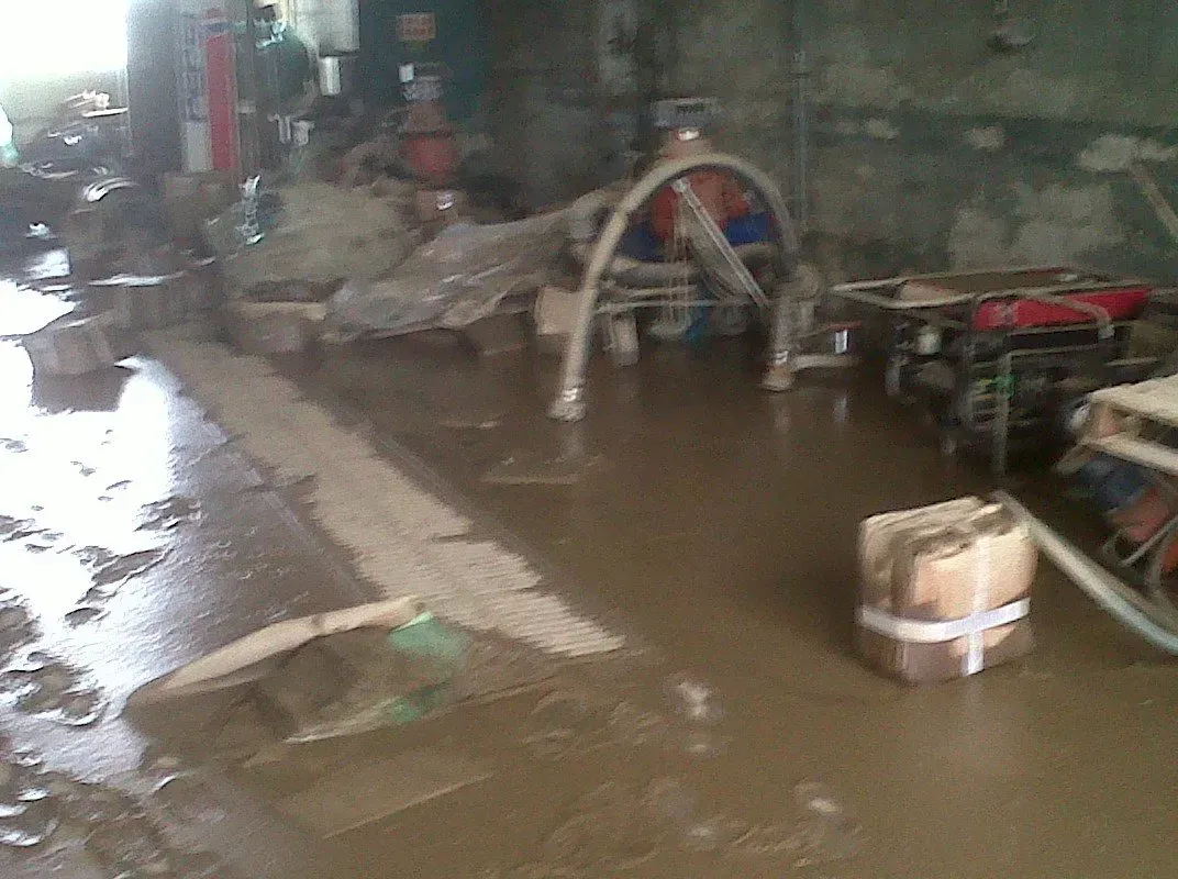 Flooded industrial space, debris in murky water. Equipment partially submerged.