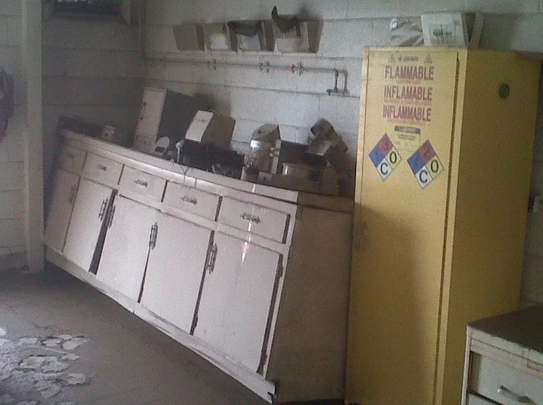 A cluttered kitchen with yellow cabinet and long countertop with cabinets, likely old, dirty.