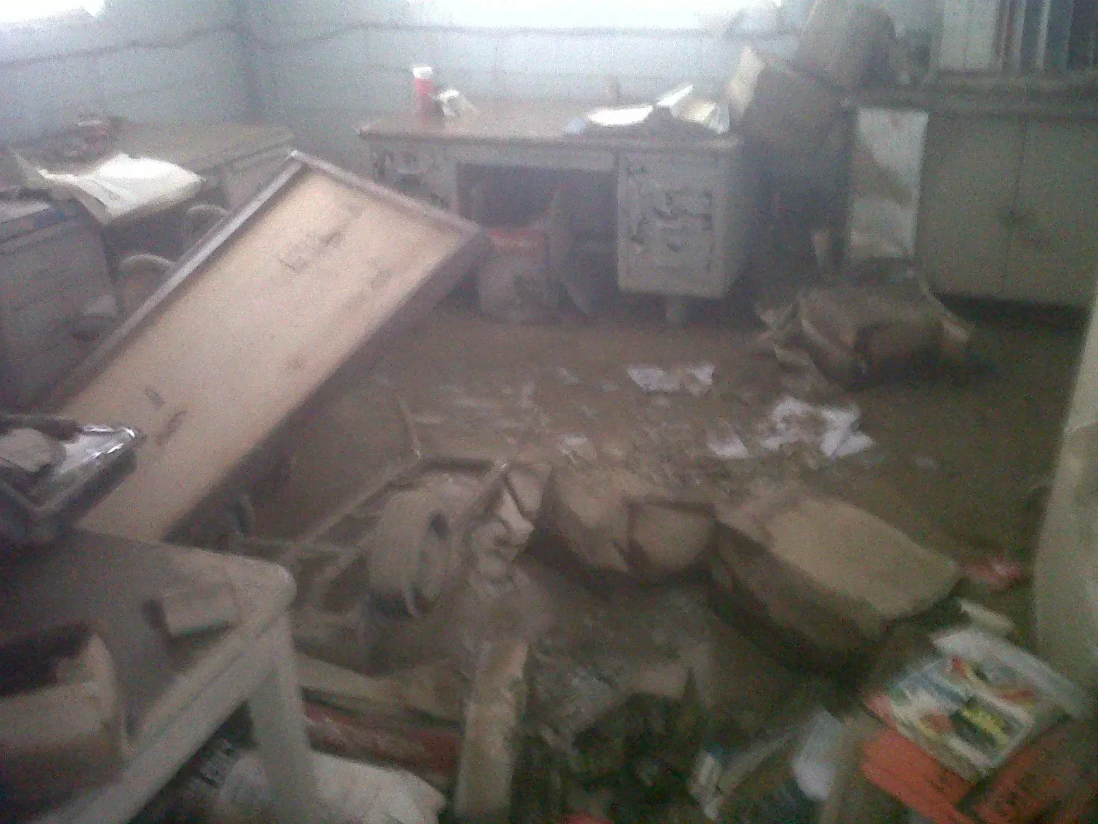 Flooded office with overturned furniture, debris, and water covering the floor.