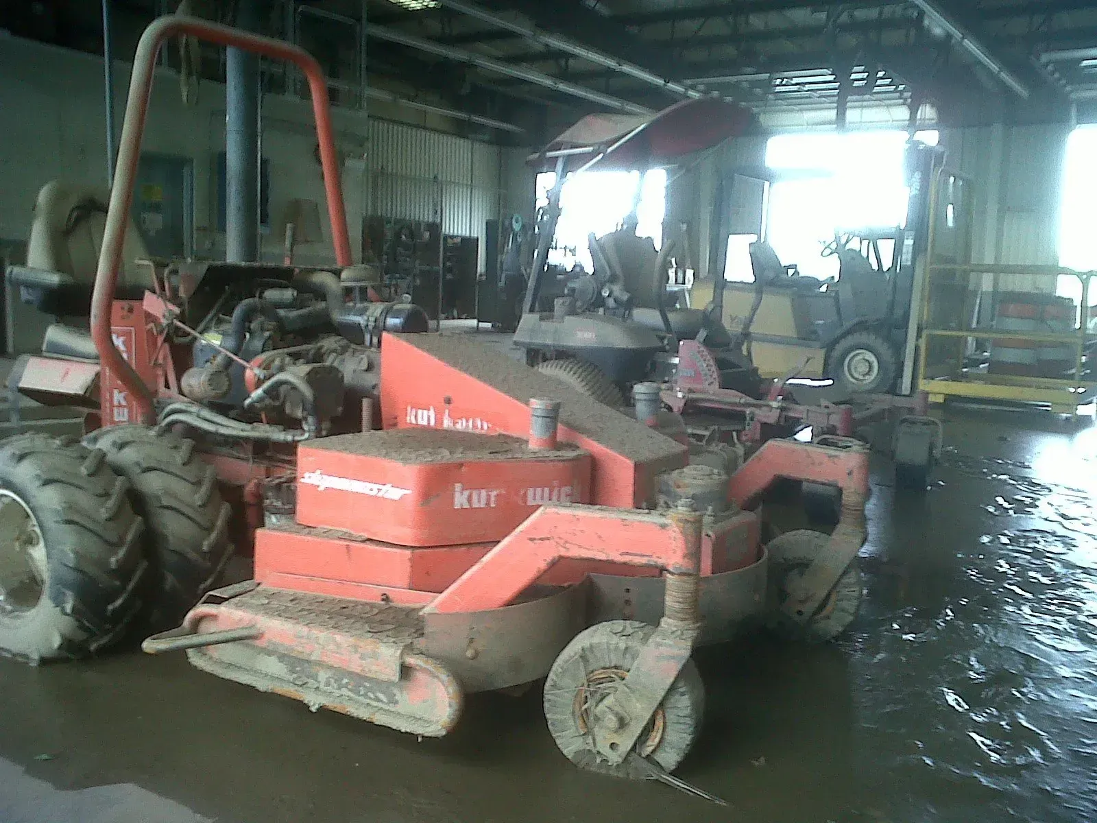Red, muddy commercial lawnmower in a flooded garage.