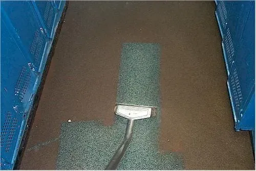 Cleaning a dark floor between blue lockers. A section of the floor has been cleaned, revealing a lighter color.