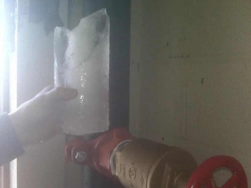 Hand holding a large chunk of ice near a fire hydrant valve.