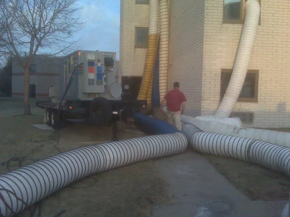 A truck with hoses attached to a building, a man walks nearby.