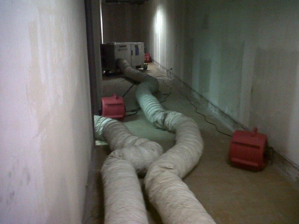 Two large hoses snaking along a concrete corridor, connected to a machine. Two red boxes are also in the corridor.