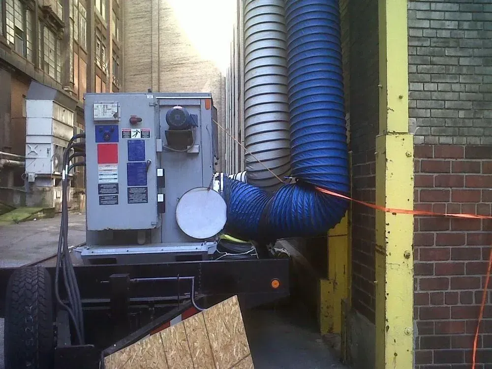 Grey machine with blue hoses on a truck, in an alley between buildings.