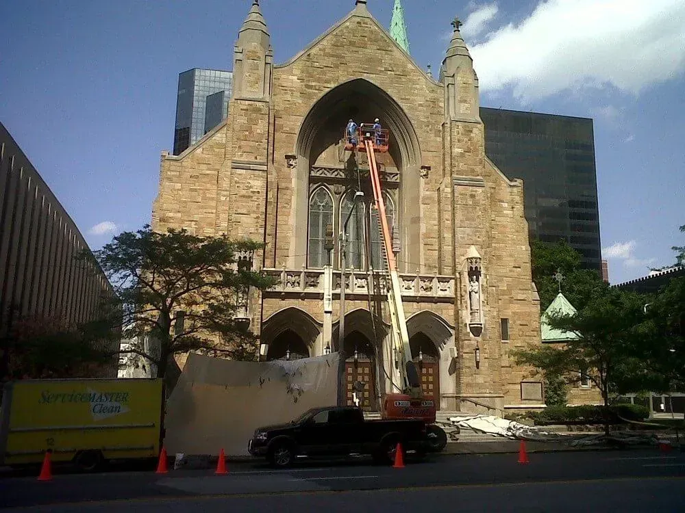 Church facade with workers in a lift, truck, and construction barriers, setting: urban street, sunny.