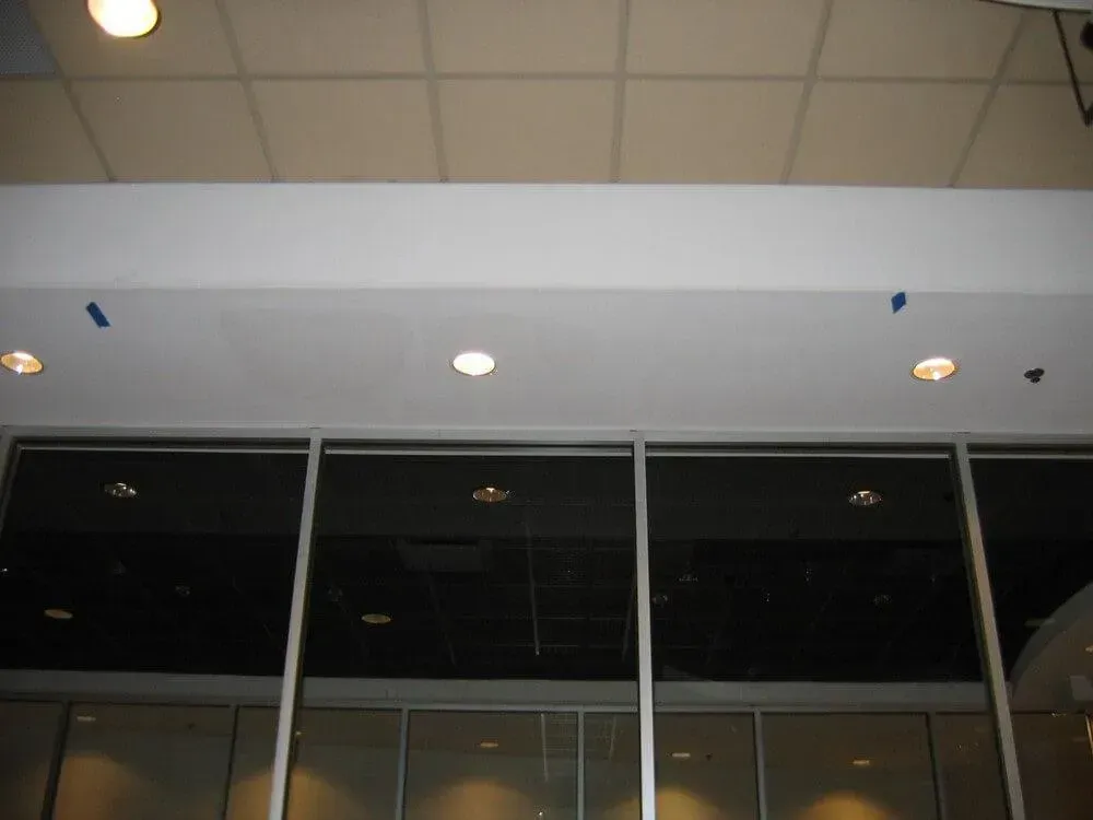 White ceiling with recessed lights above large dark windows.