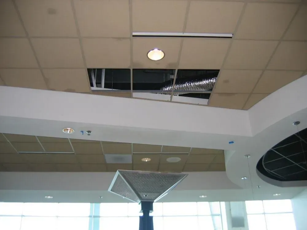 Damaged ceiling panel with a large hole revealing the structure, possibly in an indoor commercial space.