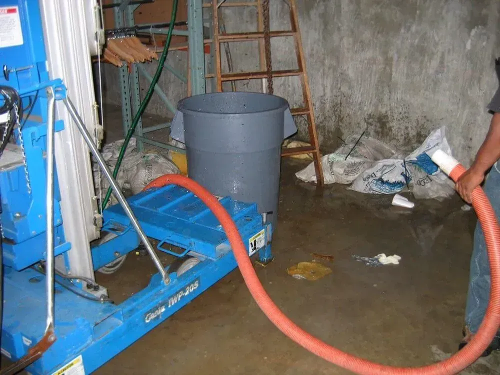 A blue lift machine pumping water out of a flooded storage room; a person holds the hose.