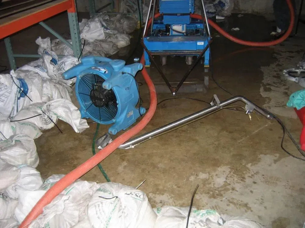 Blue fan and water extraction equipment in flooded warehouse, drying out saturated area.