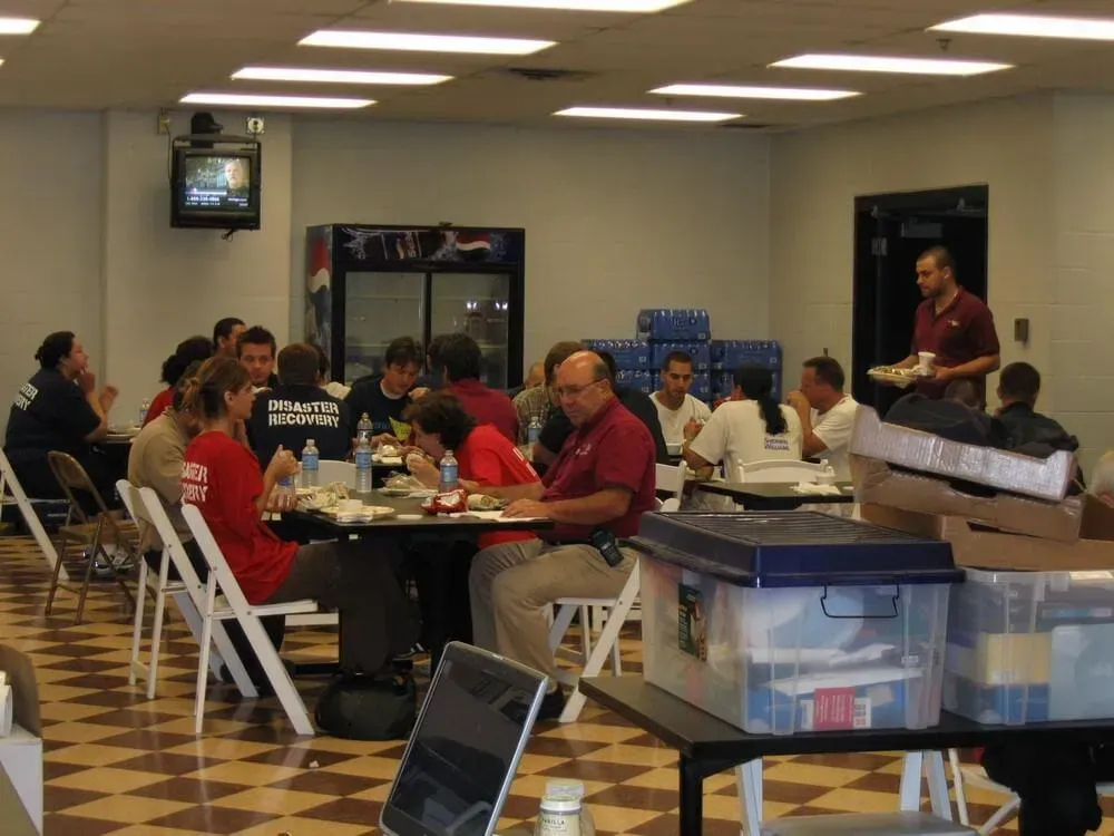 People eating at tables in a room with a cooler, TV, and water bottles.