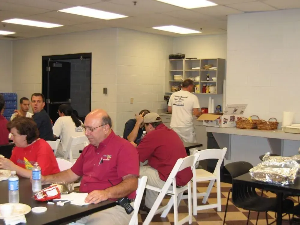 People at tables in a room, some eating, with a person behind a counter in a white shirt.