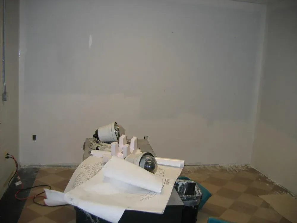 Room with gray walls and a checkered floor, construction materials on a table in the foreground.