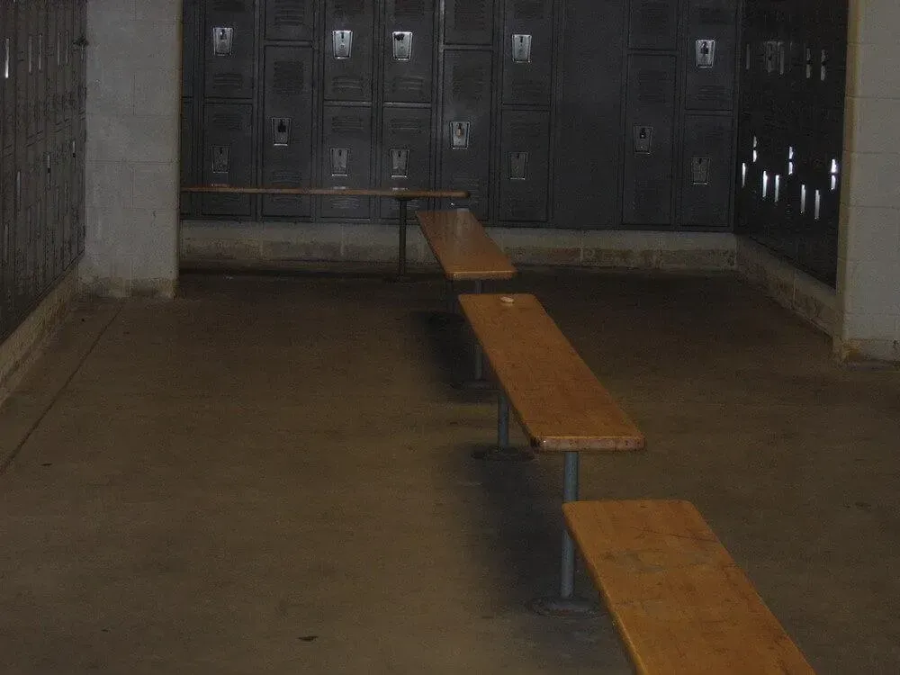 Locker room with dark lockers, wooden benches, and concrete floor.