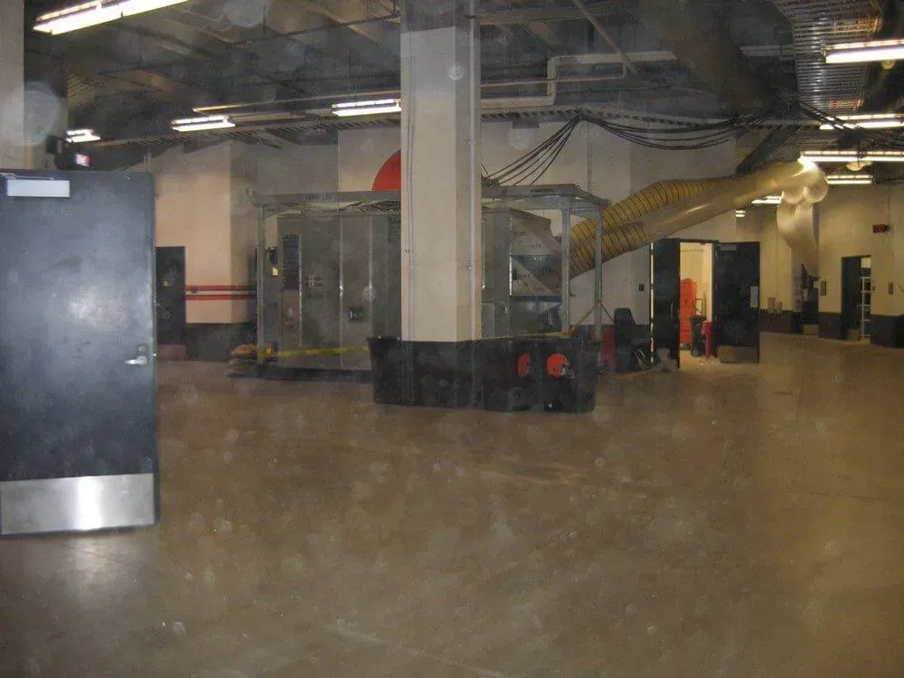 An empty, industrial space with concrete floor, metal structures, and overhead lighting.