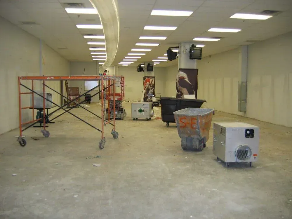 Interior of an empty commercial space under construction. Scaffolding, equipment, and bare walls are visible.