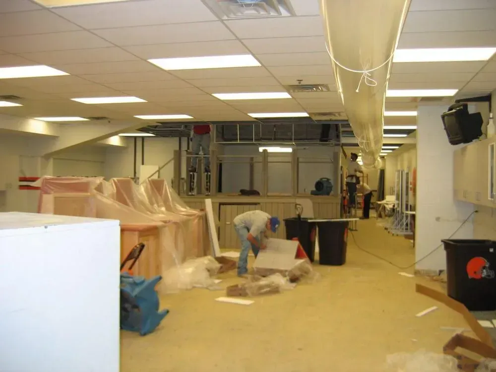 Construction in progress, interior of a commercial space with workers. Building materials and covered furniture. Fluorescent lighting.
