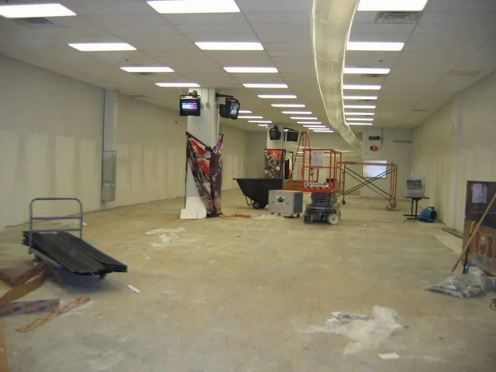 Empty retail space under construction, featuring work tools, bare walls, and overhead lighting.
