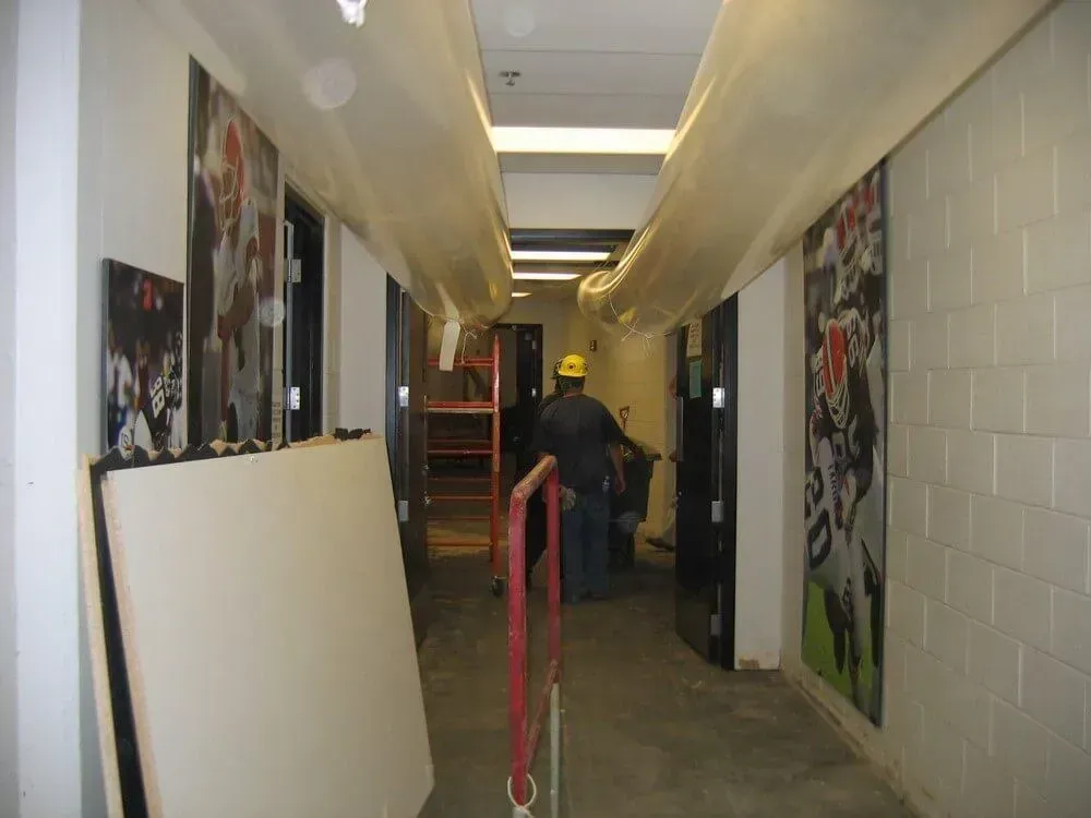 Corridor with work in progress. Worker in hard hat, ductwork, artwork, and construction materials.