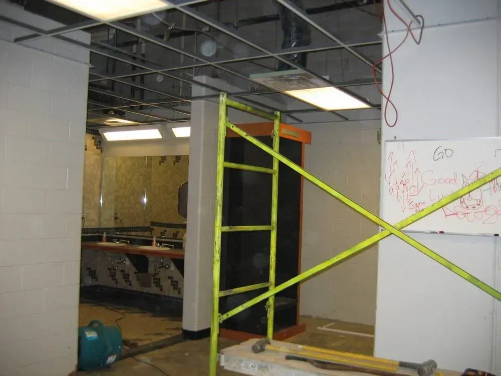Interior of a construction site with exposed ceiling grid and a yellow ladder. Walls are partially built.