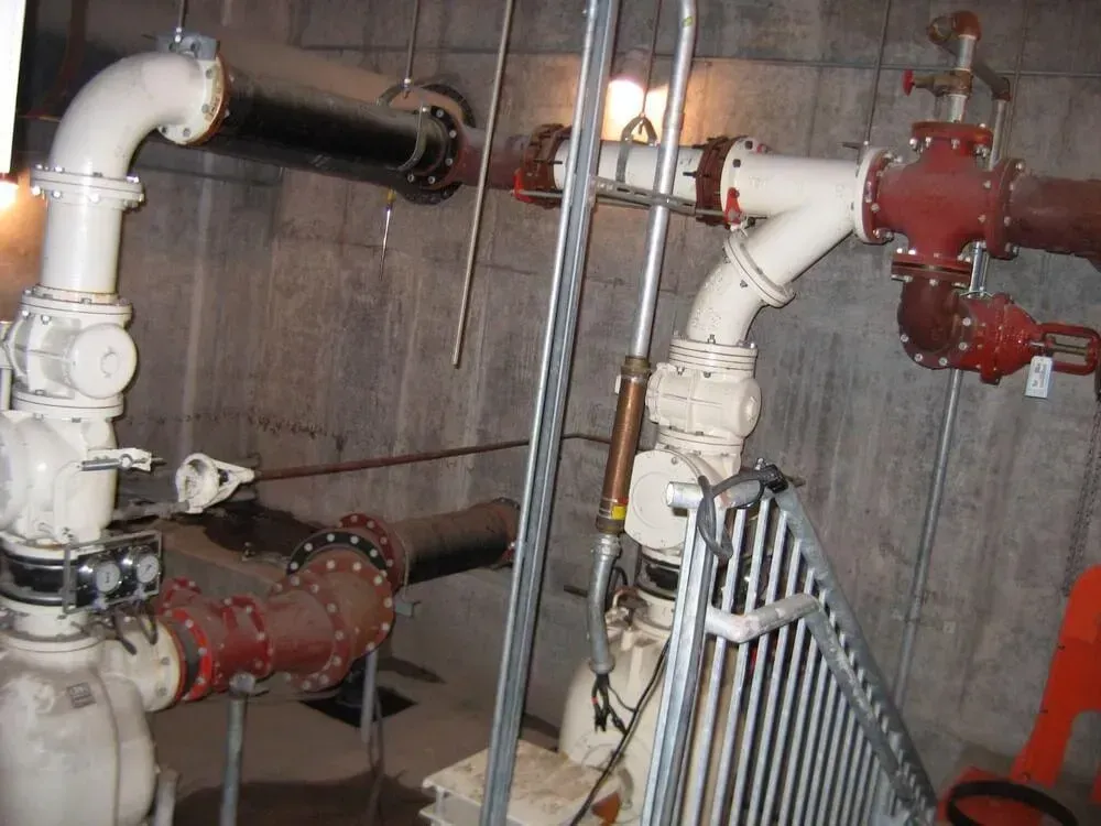 Industrial pipes and valves in a concrete room; white and red pipes, metal railing.