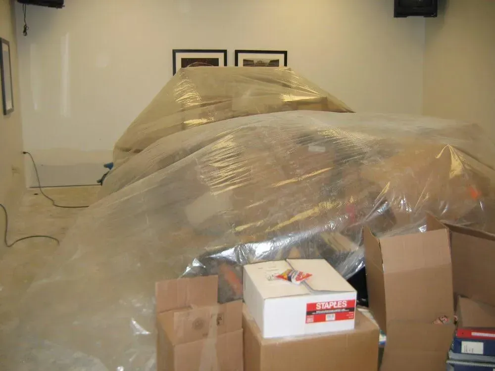 Room with furniture and boxes wrapped in plastic during a move.