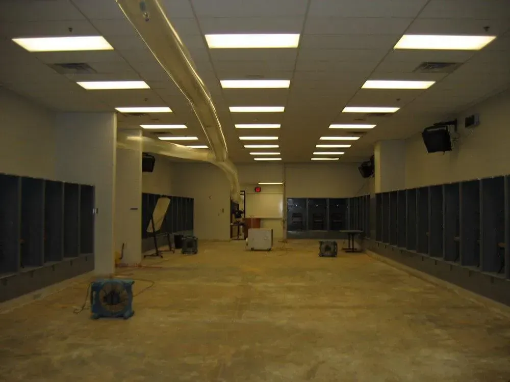 Empty room with concrete floor, fluorescent lights, and lockers along walls.