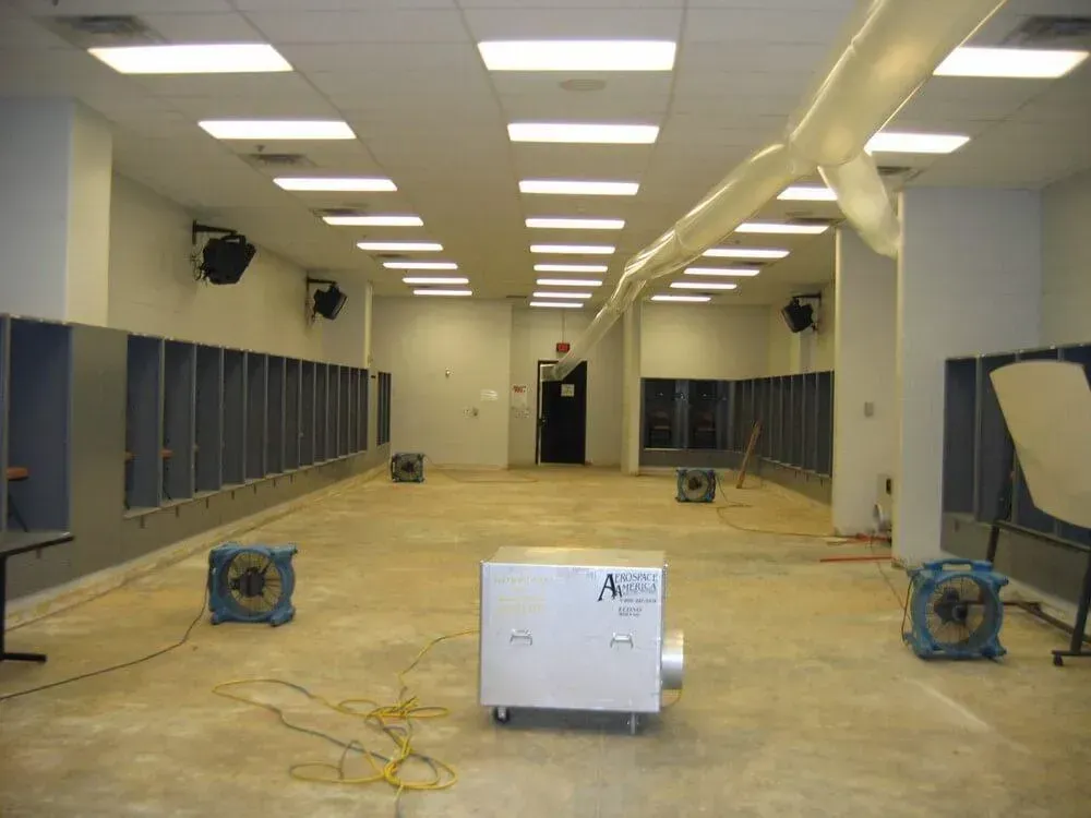 Empty locker room with industrial fans and dehumidifier, presumably for water damage remediation.