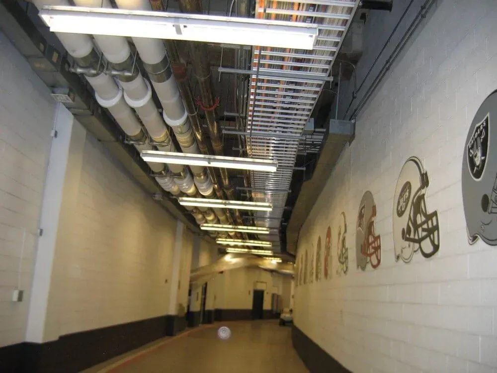 Tunnel with Raiders helmet mural, exposed pipes, and fluorescent lighting.