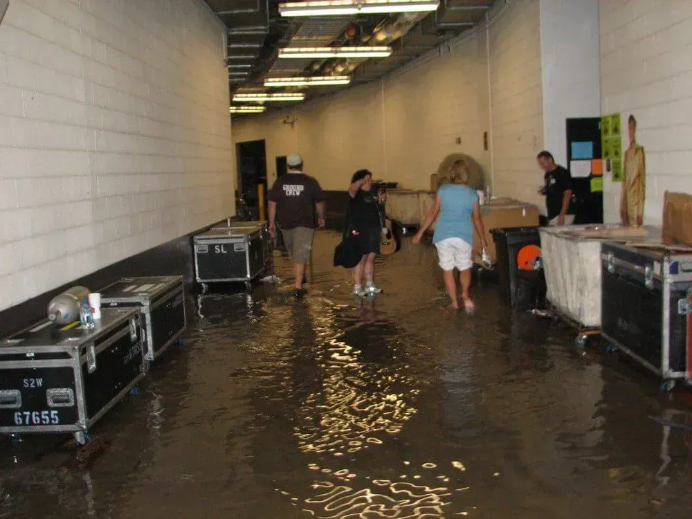 Flooded backstage hallway with several people wading through water, surrounded by equipment cases.