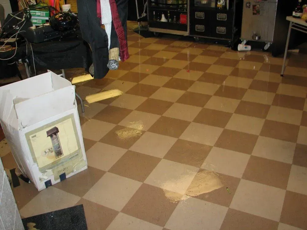 Brown and tan checkered floor with water spots; a cardboard box and person's legs in the scene.