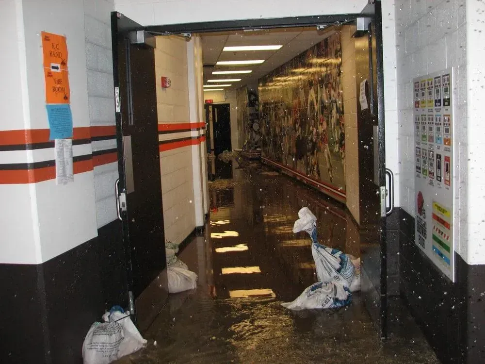 Hallway flooded with water. White ceiling lights, dark door frames, and white, black, orange wall decorations.