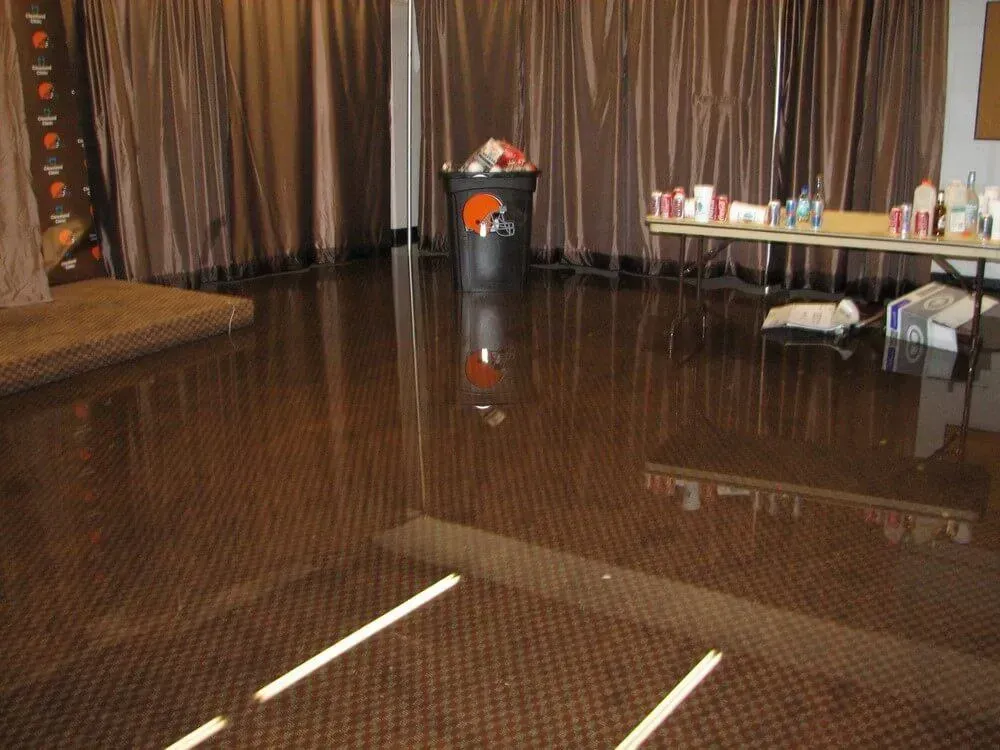 Shiny brown floor reflecting a room with brown curtains, a trash can, and a table with items.