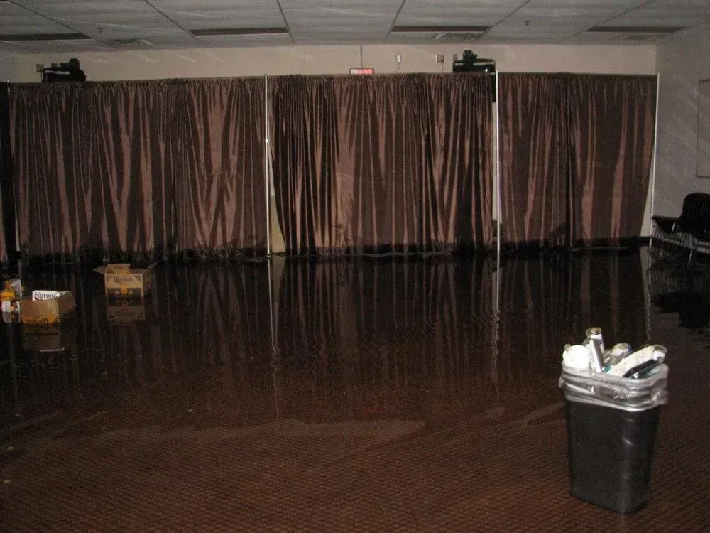Dark brown curtains backdrop a flooded room with a black trash can and cardboard boxes.