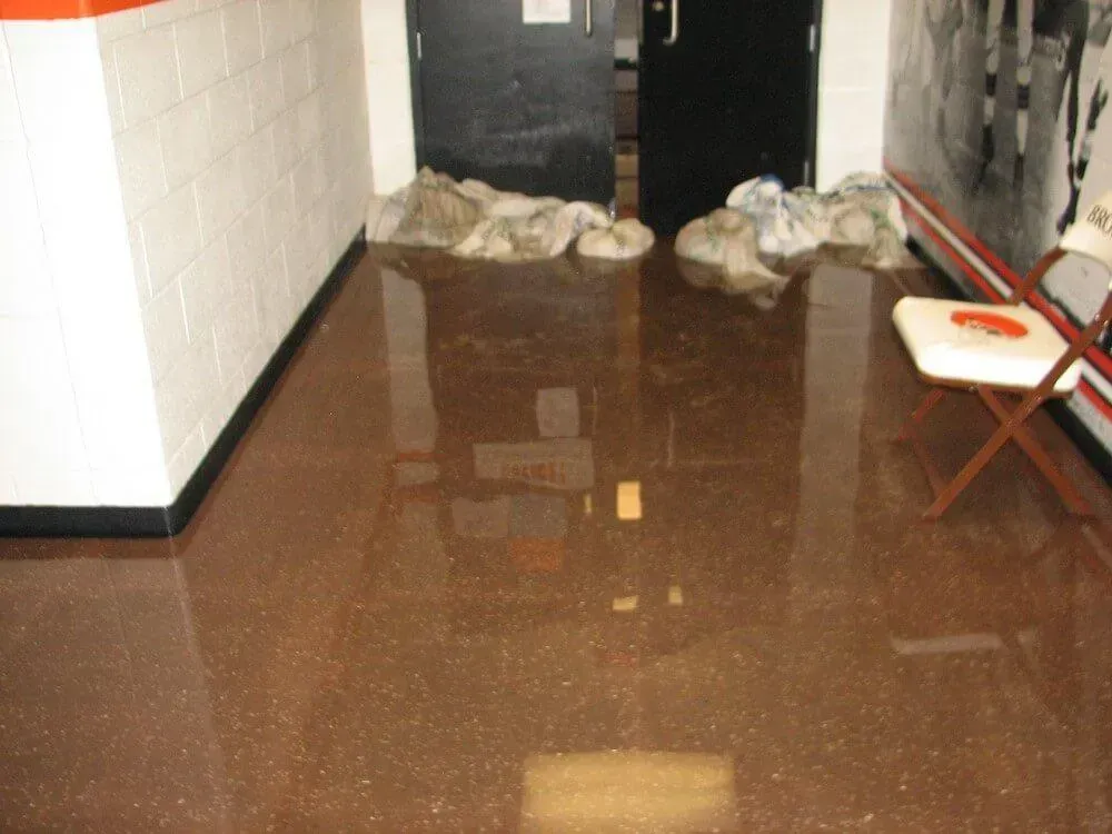 Flooded hallway with brown floor; sandbags by black doors. White and orange chair.