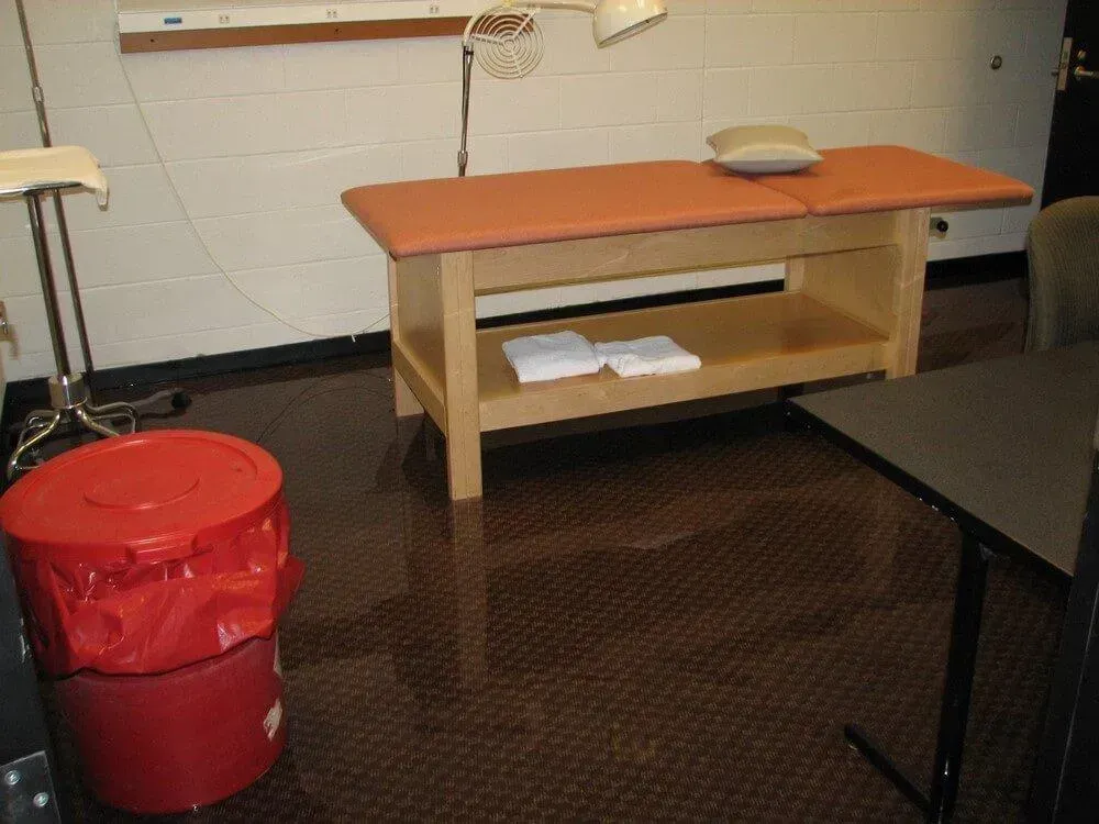 Medical exam room: Treatment table, red biohazard bin, papers, dark floor.