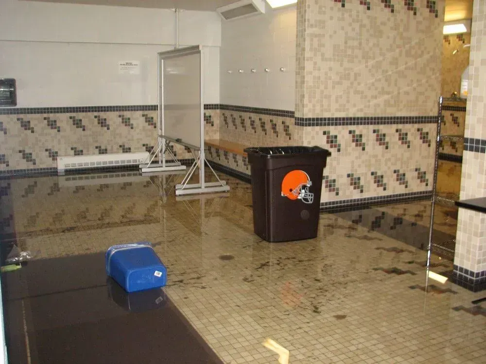 Browns locker room flooded, water on the tiled floor. A trash can with Browns logo is in the room.