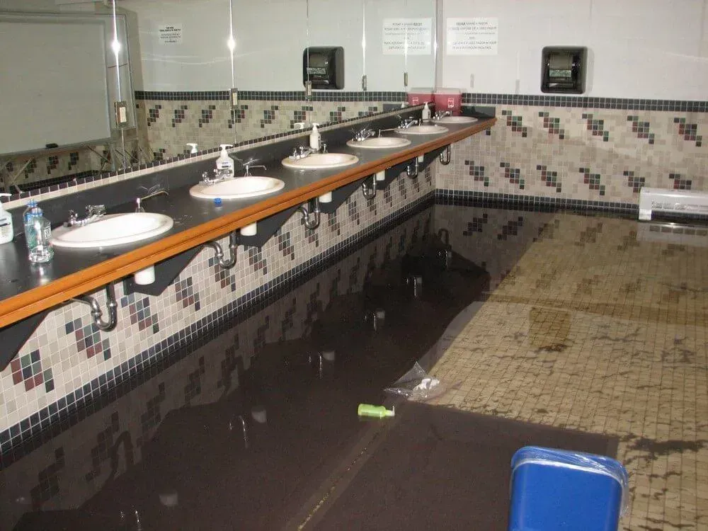 Flooded public restroom with sinks, dark water, and tiled walls.
