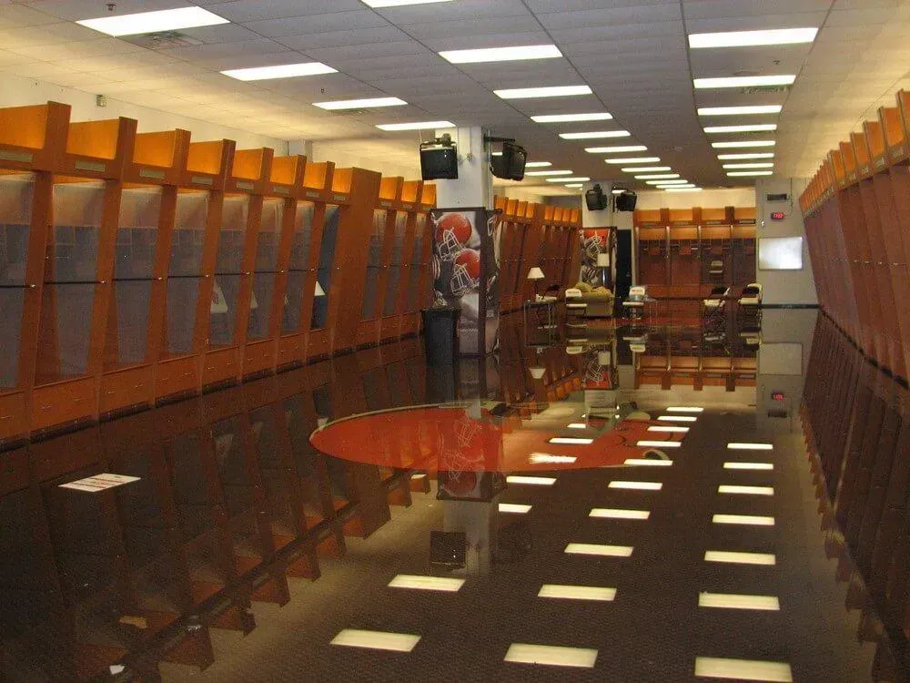 Locker room with orange lockers and glossy, reflective floor. Overhead lighting creates a grid pattern on the floor.