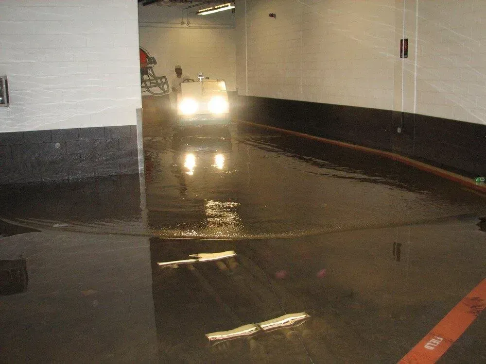 Car driving through flooded indoor area; headlights on, water reflecting lights.