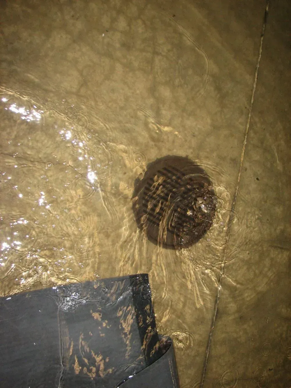 Water flowing over a round floor drain. Black tape is visible in the lower left corner.