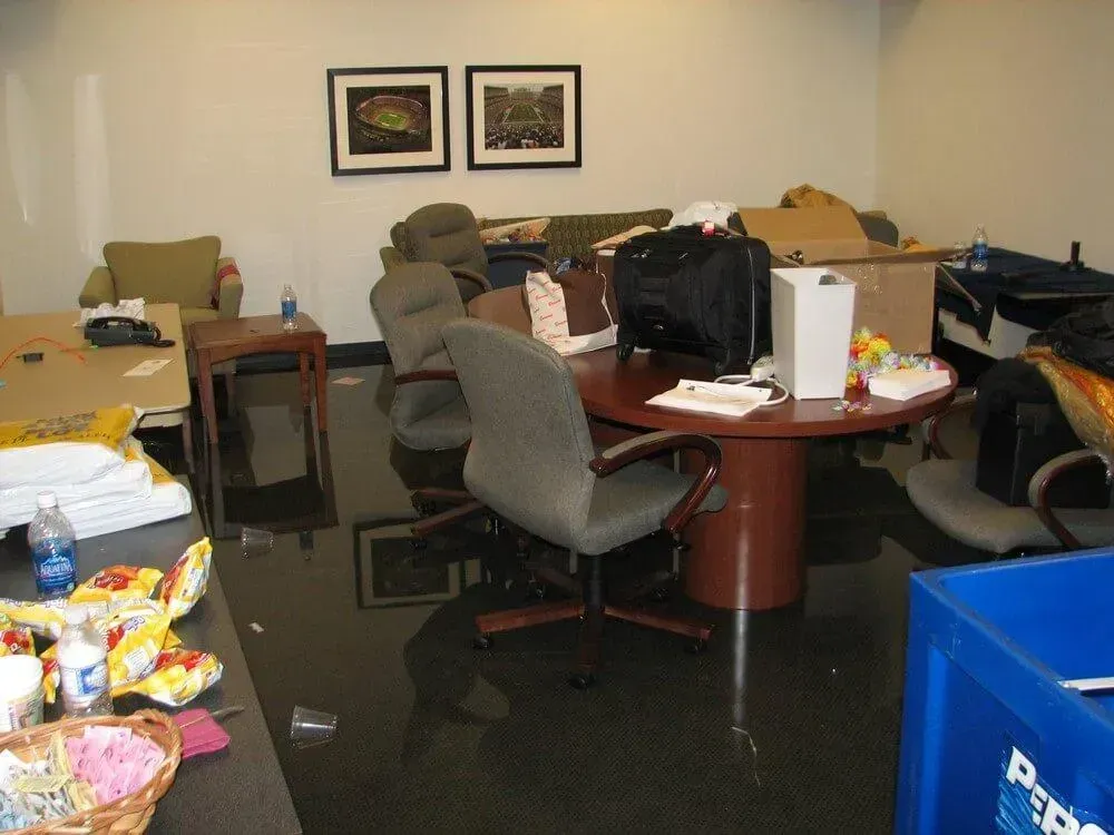 Cluttered office with dark, possibly wet, floor. Furniture and boxes are scattered around a round table.