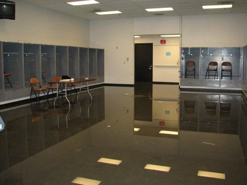 A locker room with rows of gray lockers, brown chairs, and a glossy, dark floor.
