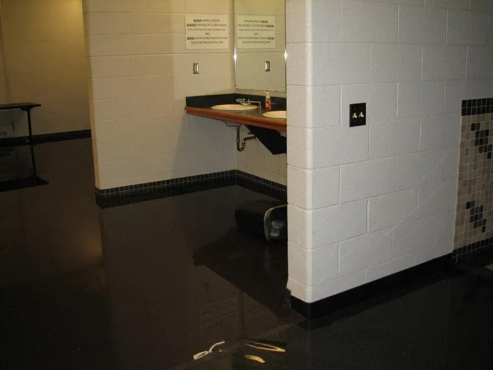 Public restroom with dark glossy floor, white brick walls, sinks, and black accents.