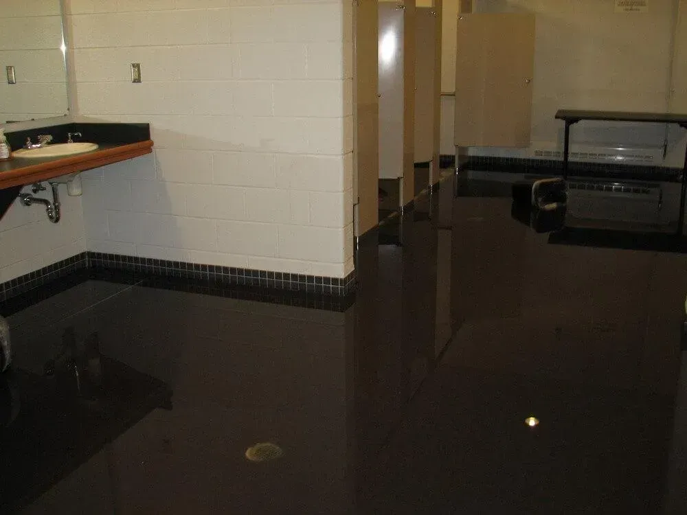 Dark, glossy floor in a public restroom with sinks, stalls, and a long countertop.
