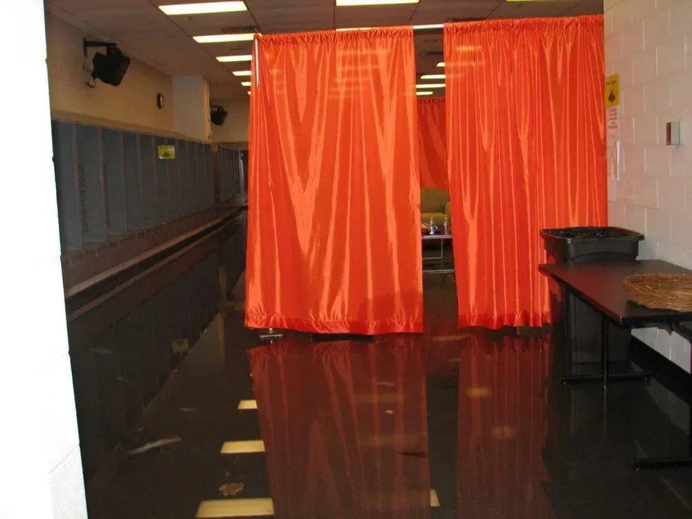 Orange curtains divide a room with a shiny black floor. A table sits to the right.