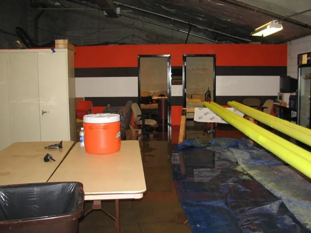 Interior shot of a flooded room with tables, water cooler, and doors leading to other rooms; walls are orange and black.