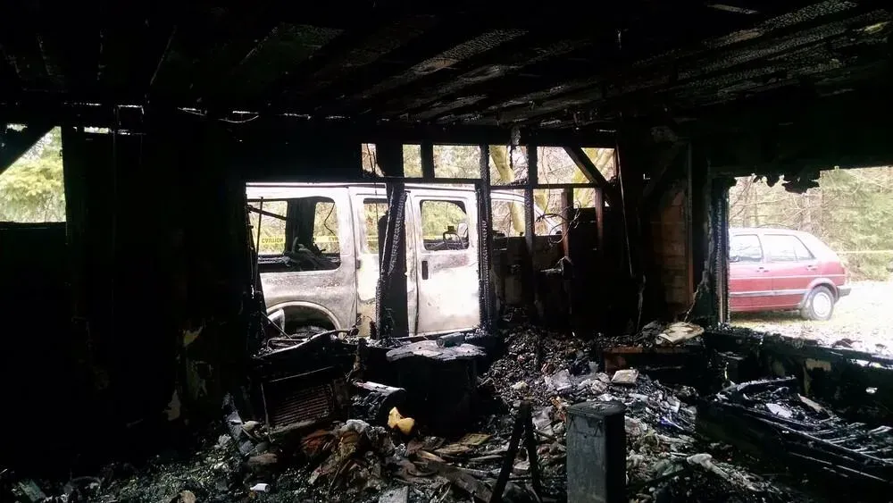 Interior view of a building destroyed by fire; a van is visible through the doorway and another car is parked outside.