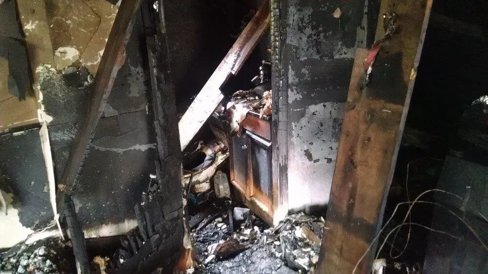 Charred interior of a building after a fire, with black, burnt wood and debris.